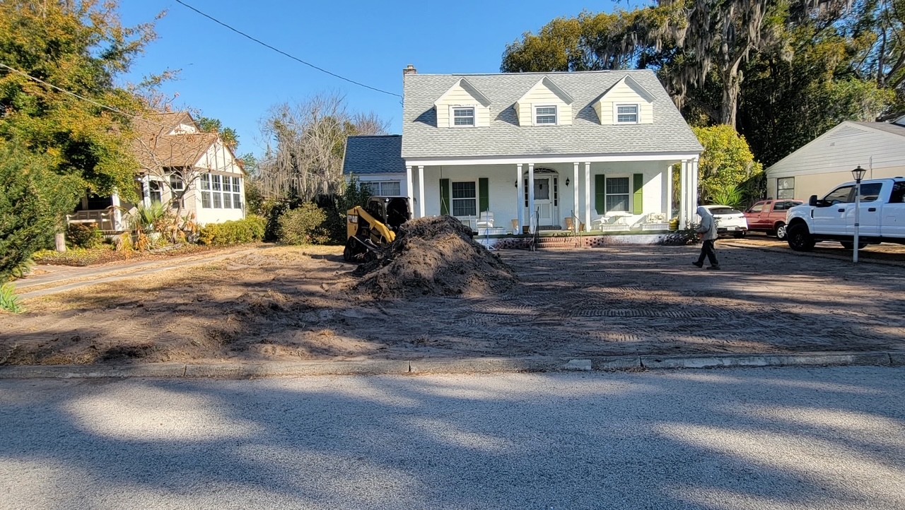 Skid steer grading a residential driveway and yard with a fresh load of fill dirt